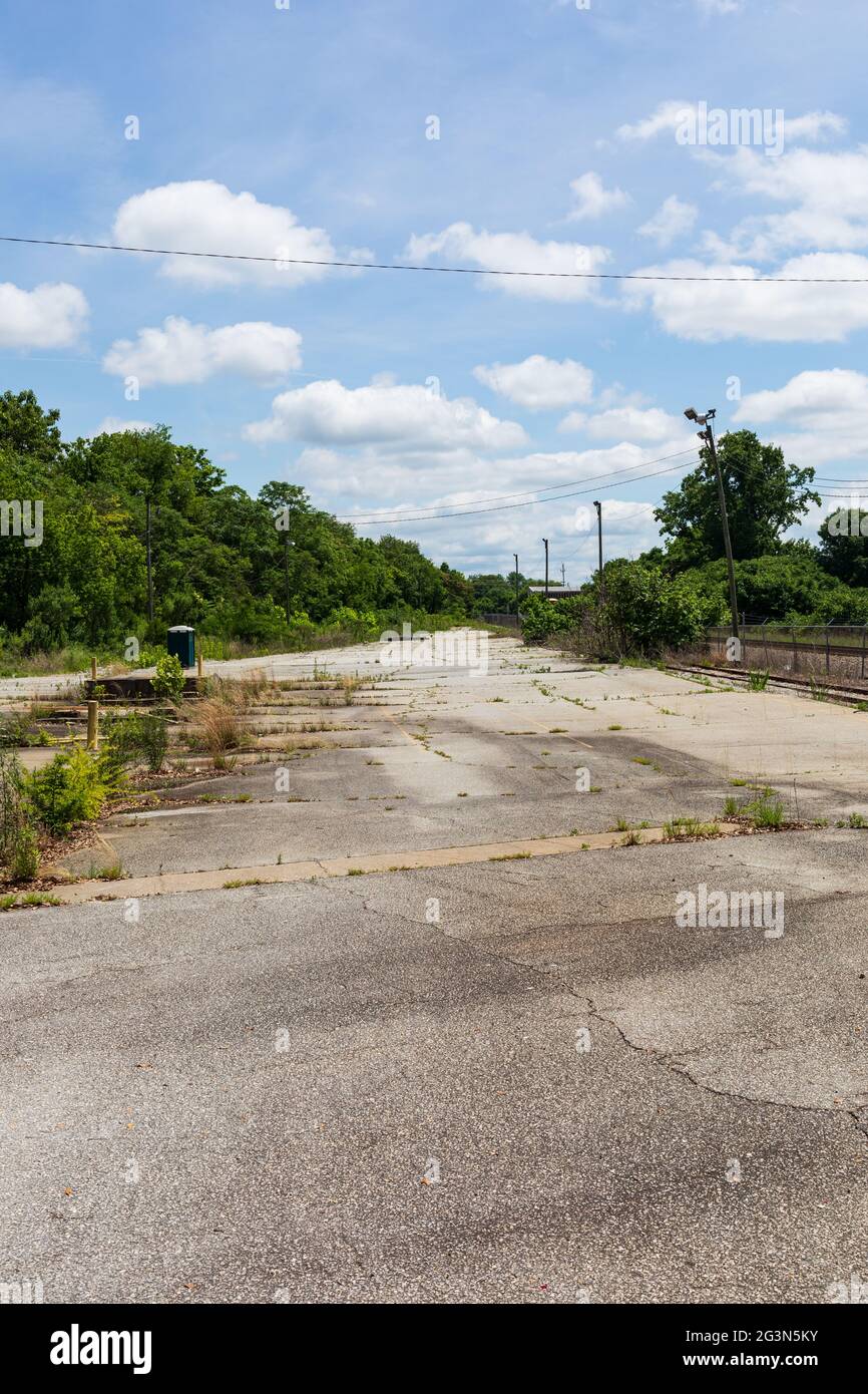 SPARTANBURG, SC, USA-13 JUNE 2021: Vertical image. Abandoned parking lot, diminishing perspective, with greenery.  Portable toilet in distance. Broken Stock Photo