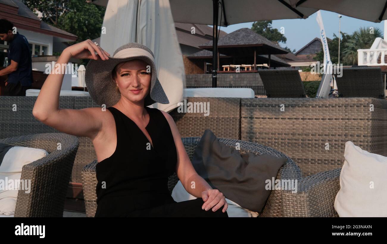 Eastern European Caucasian woman middle aged blonde hair light skin pale complexion in black dress gray straw hat outside summer time sitting Stock Photo