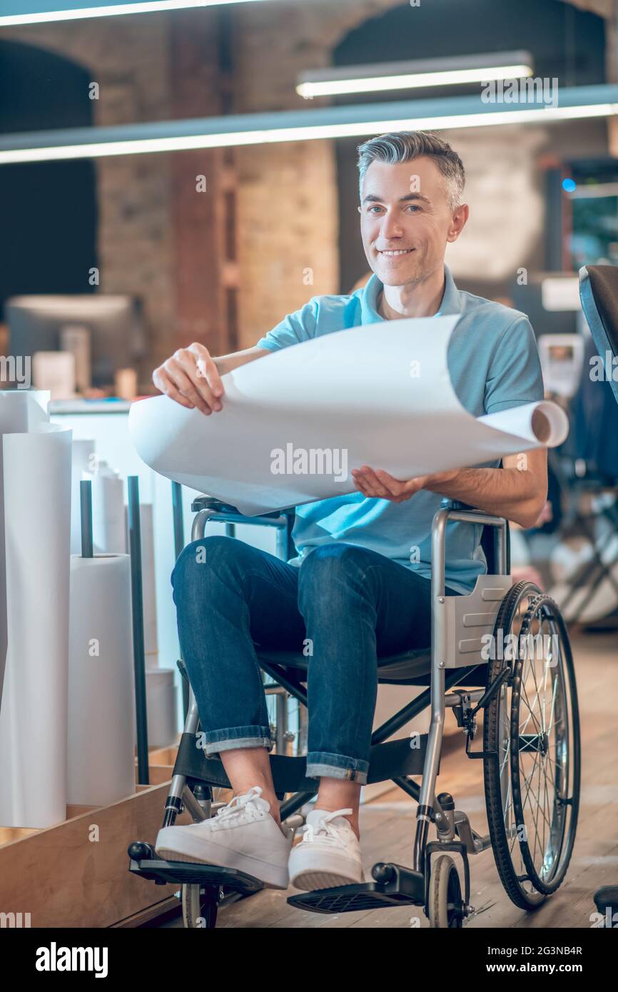 Smiling man in wheelchair with roll of paper Stock Photo
