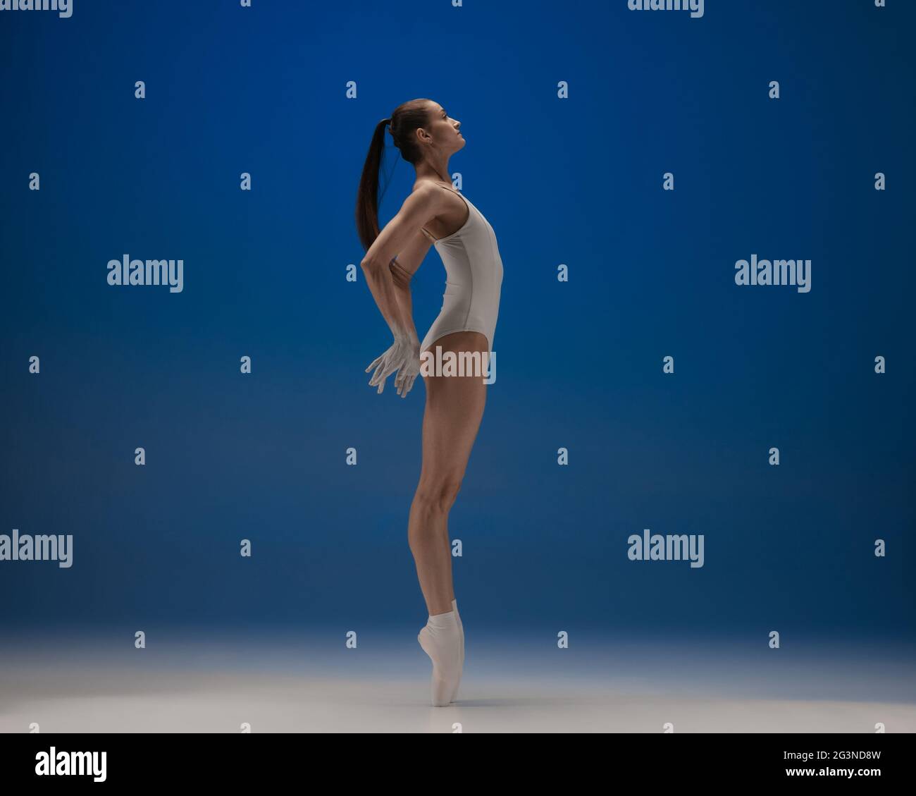 On the tips of toes. Young beautiful ballerina in action isolated over blue background. Stock Photo