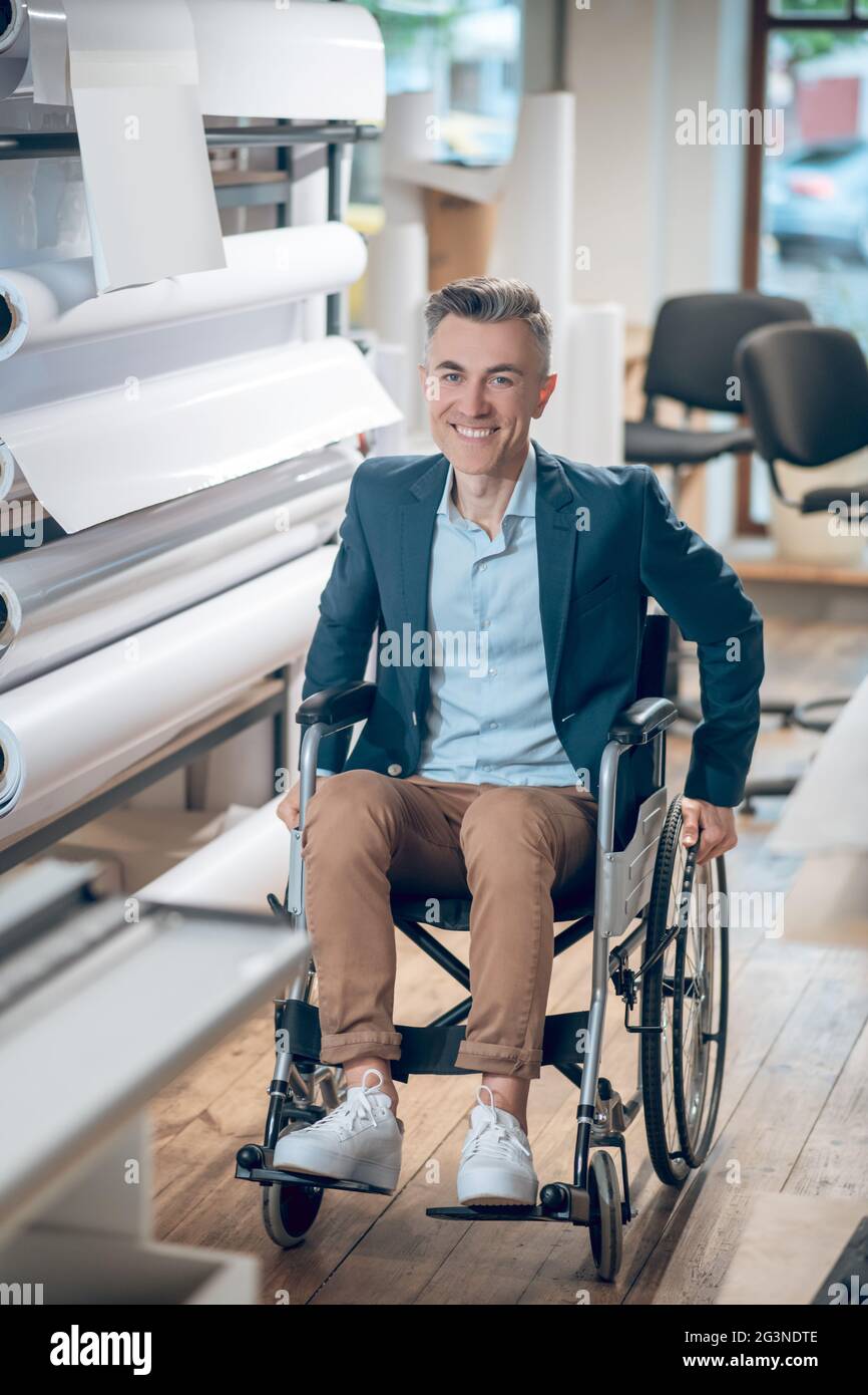 Smiling man on wheelchair near rolls of paper Stock Photo