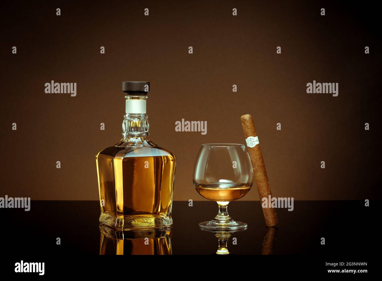 close up view of cigar, bottle of cognac and a glass aside on color back. Stock Photo