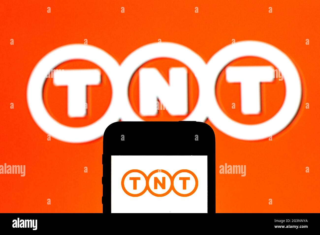 In this photo illustration a TNT Express logo seen displayed on a smartphone with a TNT Express logo in the background. Stock Photo
