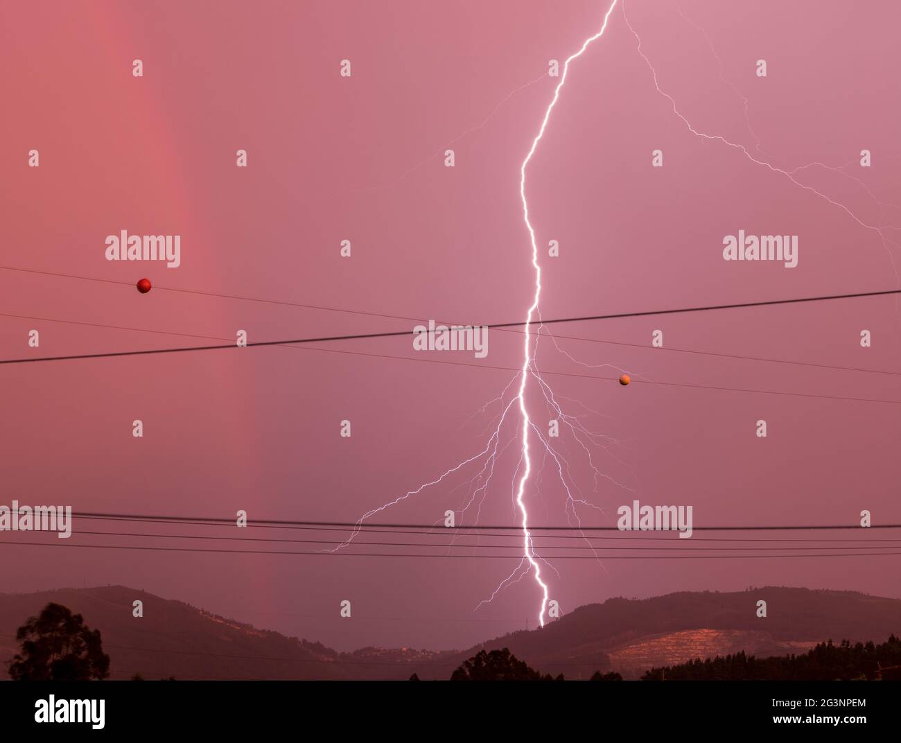 Lightning strike, rainbow and red tones skies in a stormy afternoon Stock Photo