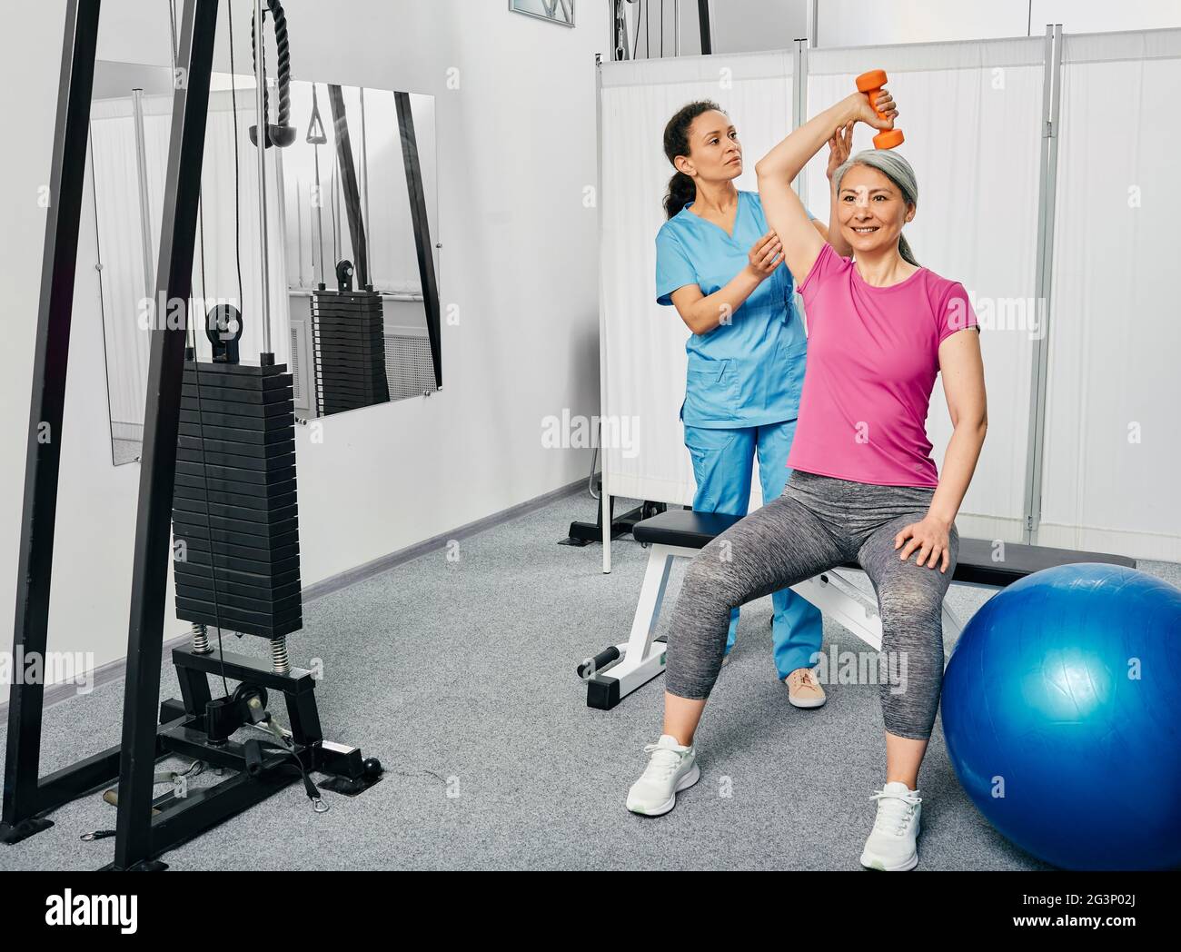 Physical therapy. Mature woman lift a dumbbell, she doing treatment exercise with her physiotherapist Stock Photo