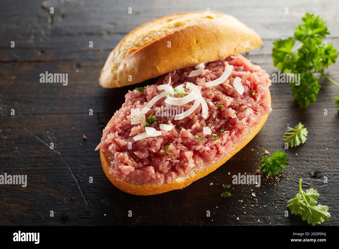 From above of tasty Mett with minced pork and onion on bread roll served on wooden table with green parsley Stock Photo