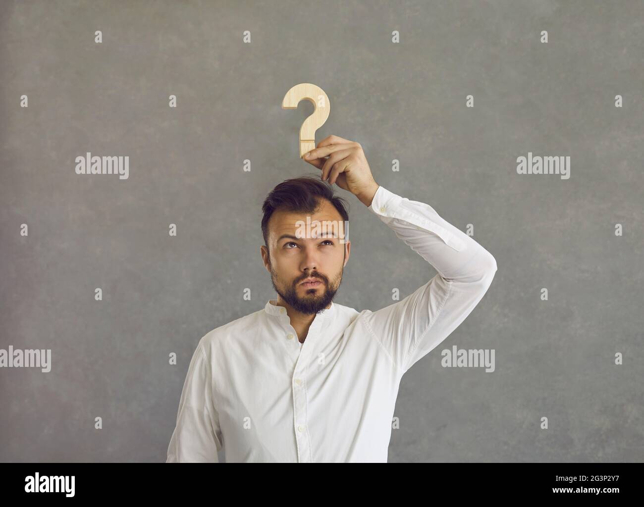 Confused man holding a question mark and thinking of an answer to a difficult question Stock Photo