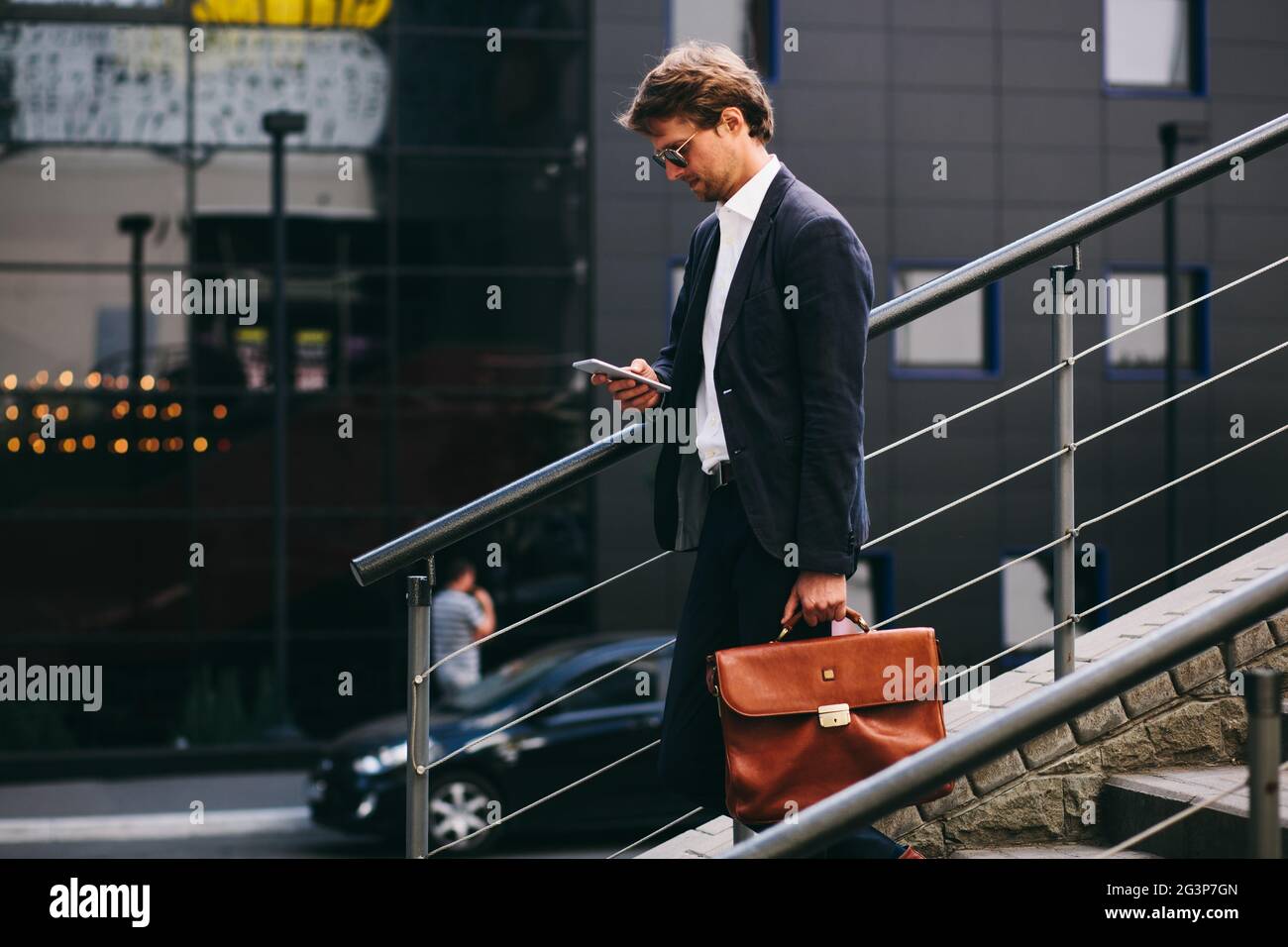 A Banker In A Stylish Suit With A Cell Phone Is Going Down The Stairs Stock Photo