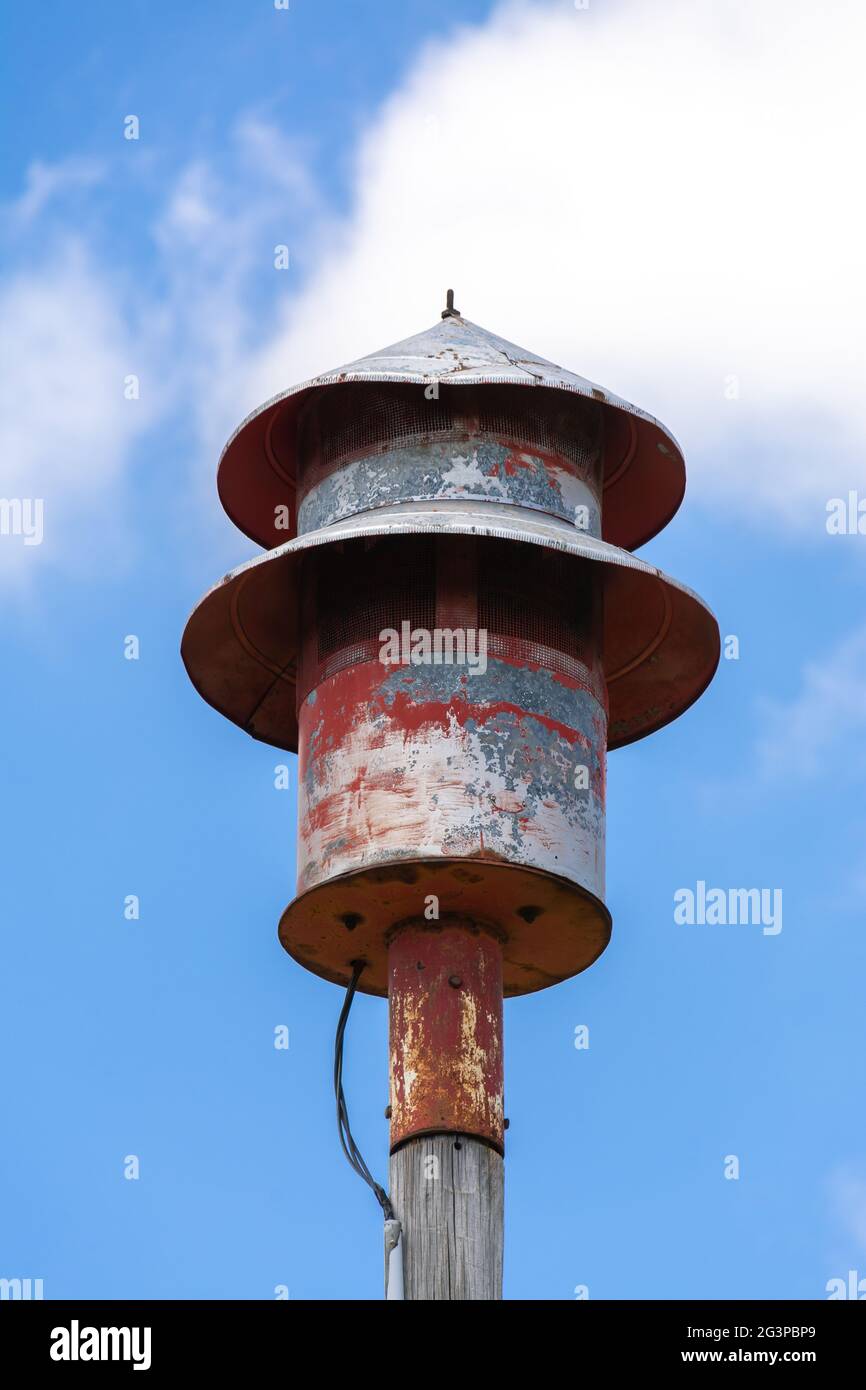 Old tornado siren in small Midwest town with blue skies and clouds in