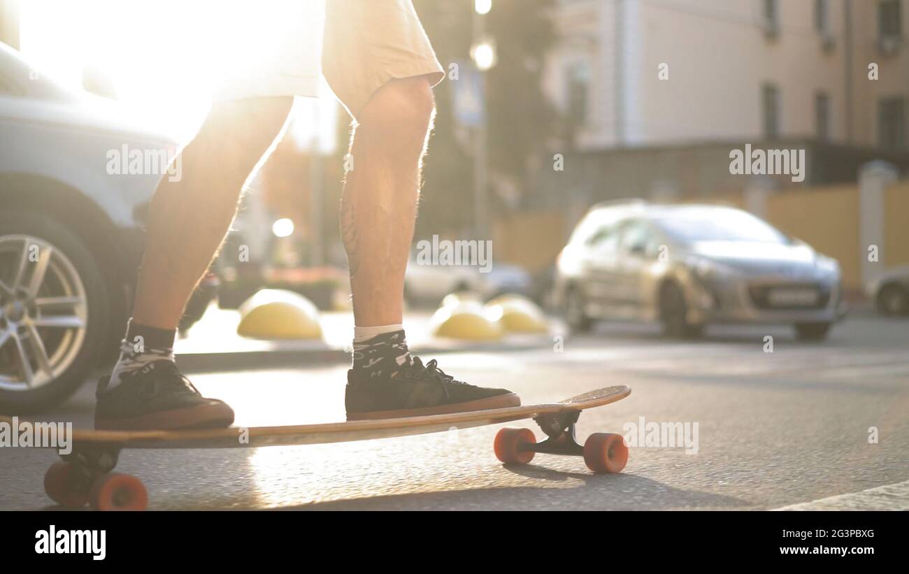 Light-skinned skater enjoys longboard ride on sunny city street Stock Photo