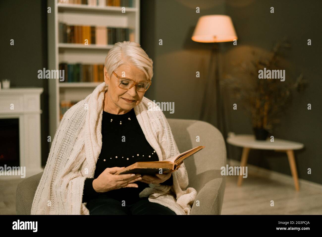 Wise Senior Woman In Eyeglasses Reads Old Book Stock Photo