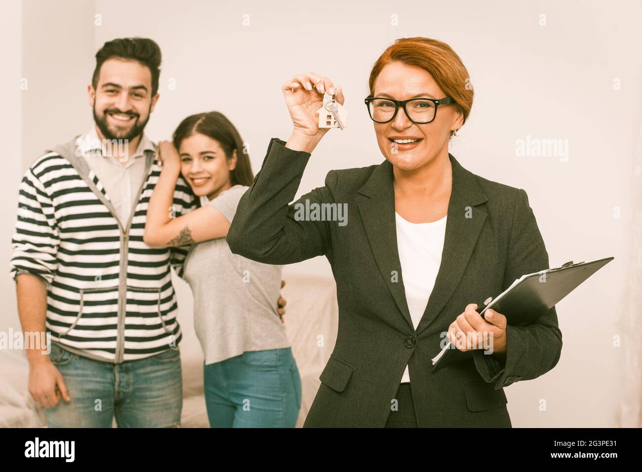 Real estate agent handls keys from new apartment rented to happy young couple. Stock Photo