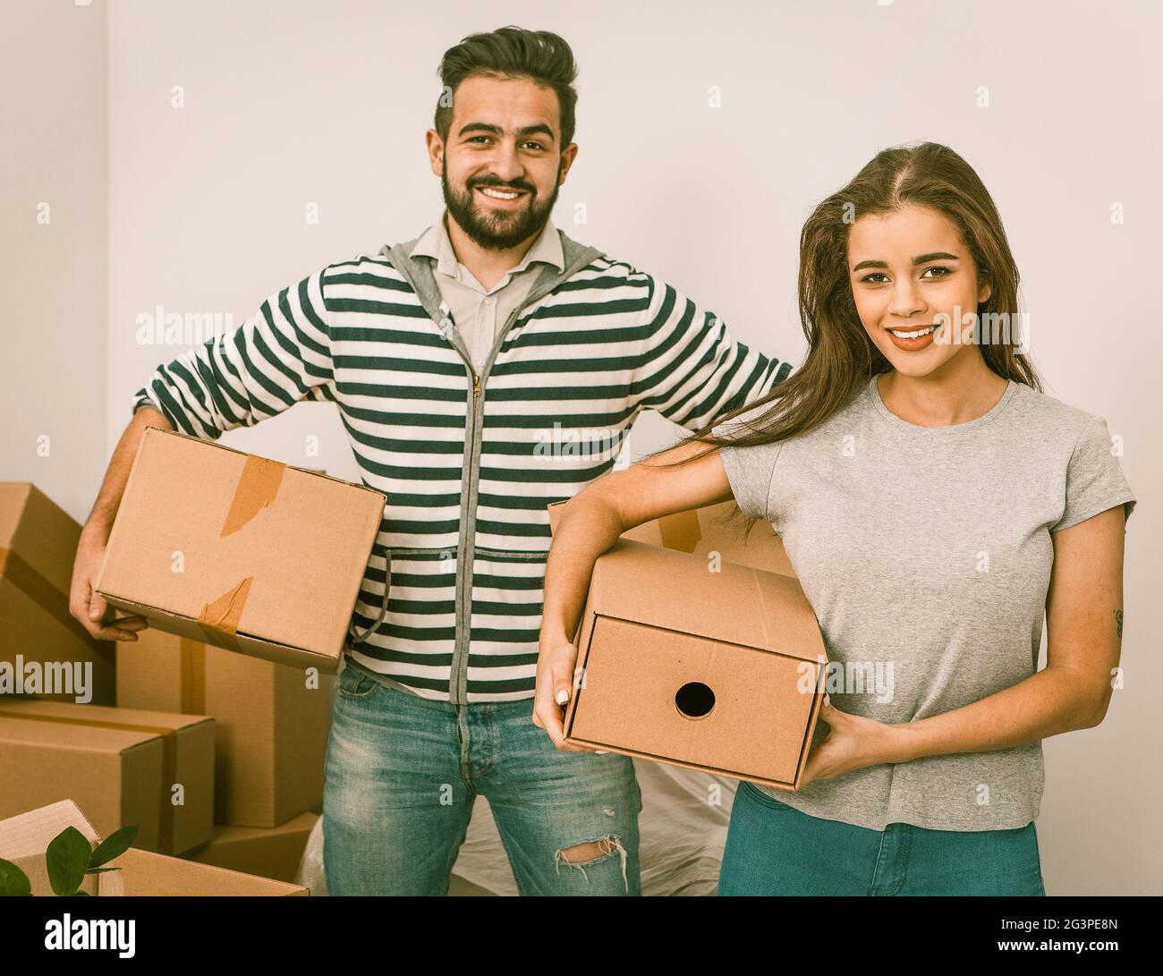 Young couple smiling and holding boxes while standing among unpacked boxes Stock Photo