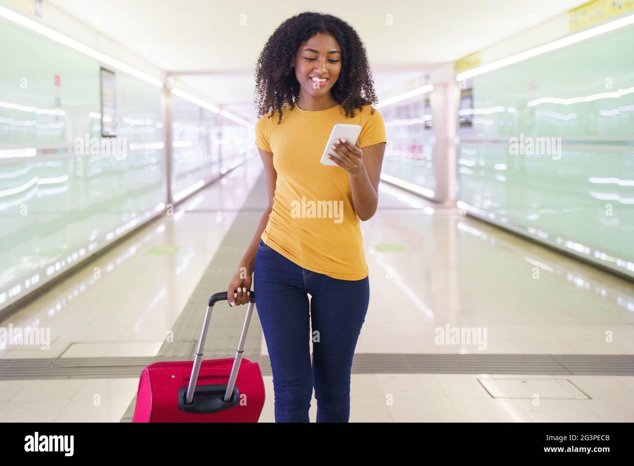 Black woman with cell phone and carryon baggage in station Stock Photo