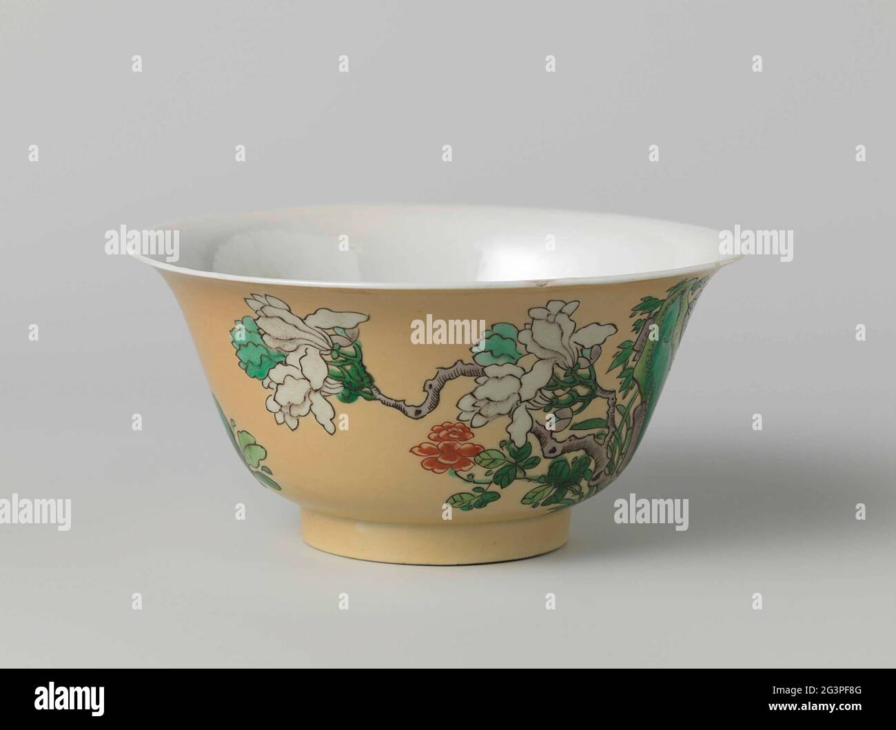 Bell-Shaped Bowl With Undergle Light Brown With Rocks and Flowers. Bell-shaped bowl of porcelain, painted in underglaze blue and on the glaze red, green, eggplant, black and white with rocks and flowers against a background of cafe-au-lait. The outside of the bowl with rocks and blooming magnolias and peonies; The inside of the bowl is with a single peony. On the underside, the six-character brand of emperor Chenghua is in a double circle in underglaze blue. A chip in the edge. Famille Verte with a brown glaze. Stock Photo