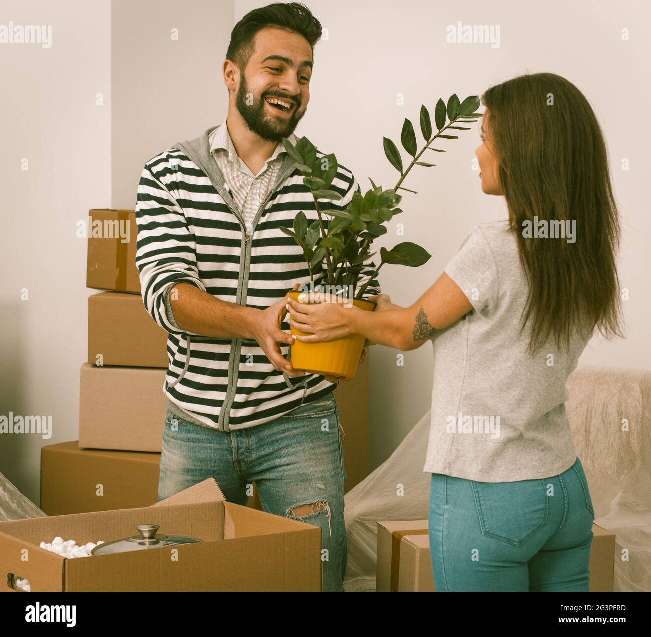 Excited young couple moving home standing close together with plants in their hands. Stock Photo