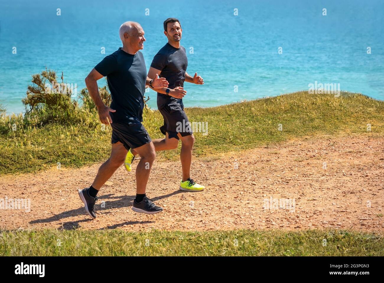 Fitness instructor gives instructions to an elderly man, a retired client, jogging on the seashore, endurance training. Stock Photo