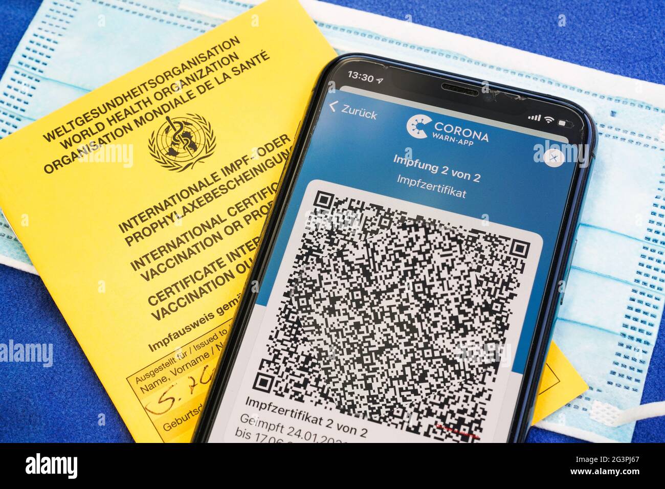 QR-Code, das digitale Impfzertifikat in der Corona Warn-App auf einem Smartphone bestätigt eine abgeschlossenen Impfung gegen Covid-19. Liegt auf dem gelben Internationalen Impfbescheinigung, Impfpass. - ACHTUNG! QR-Code und persönliche Angaben sind unkenntlich gemacht! Stock Photo