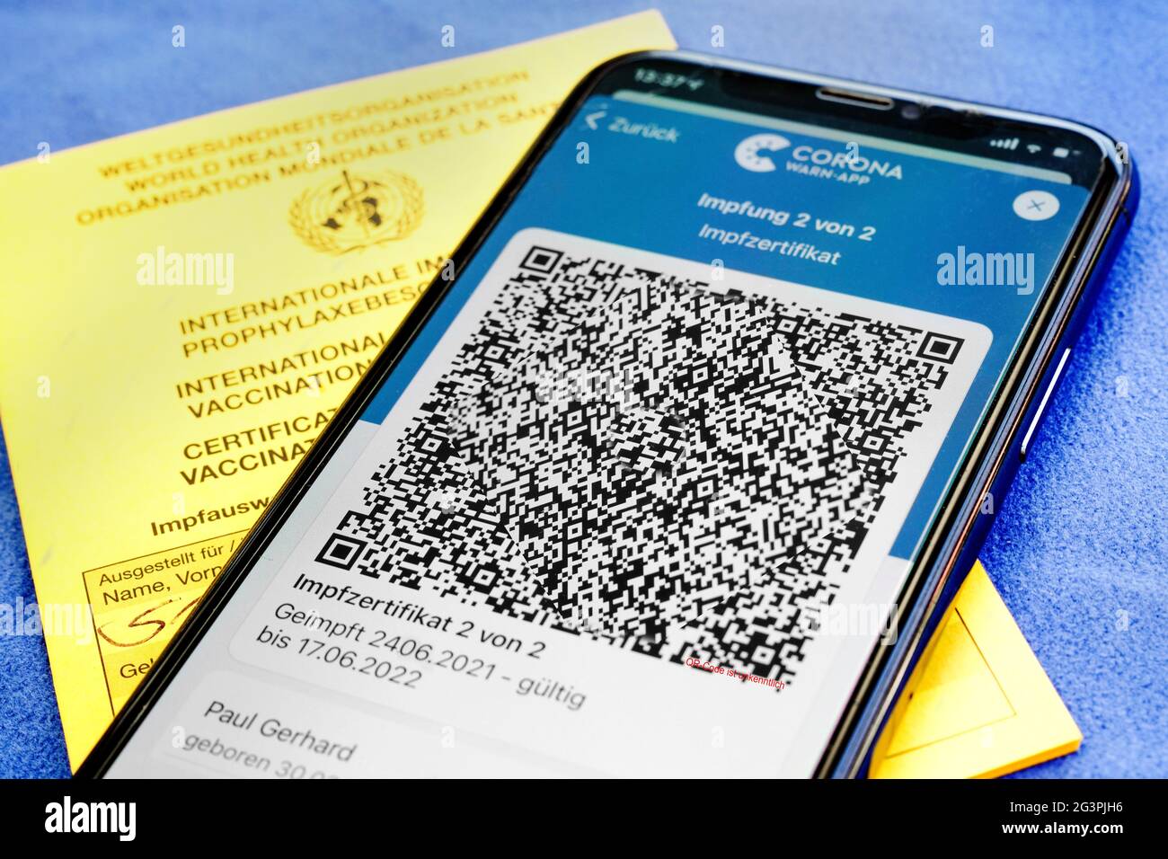 QR-Code, das digitale Impfzertifikat in der Corona Warn-App auf einem Smartphone bestätigt eine abgeschlossenen Impfung gegen Covid-19. Liegt auf der gelben Internationalen Impfbescheinigung, Impfpass. - ACHTUNG! QR-Code und persönliche Angaben sind unkenntlich gemacht! Stock Photo