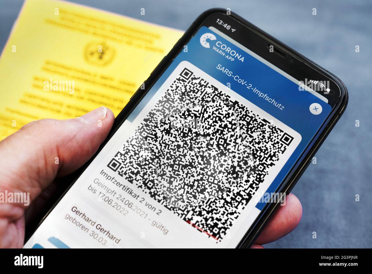QR-Code, das digitale Impfzertifikat in der Corona Warn-App auf einem Smartphone bestätigt eine abgeschlossenen Impfung gegen Covid-19. Liegt auf der gelben Internationalen Impfbescheinigung, Impfpass. - ACHTUNG! QR-Code und persönliche Angaben sind unkenntlich gemacht! Stock Photo