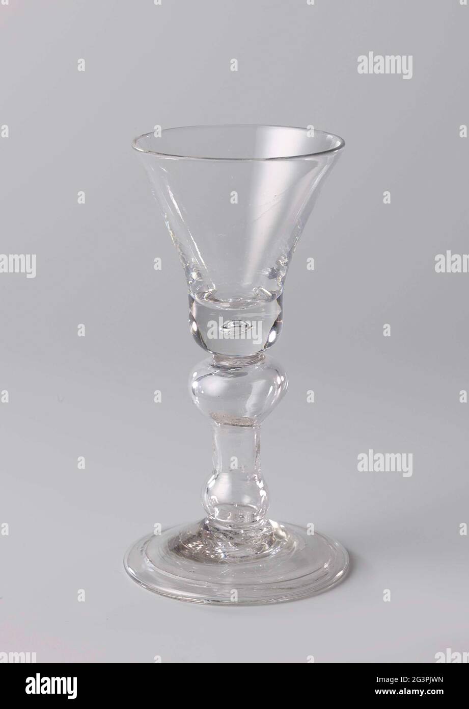 Kelkglas with an enclosed coin from 1713. Chalie glass on a conical foot with a hollow bumped edge. Holle Balustroid stem with a coin from silver from Queen Anne from the year 1713. Bell-shaped chalice with a thick bottom in which an air bubble has been inserted. Stock Photo