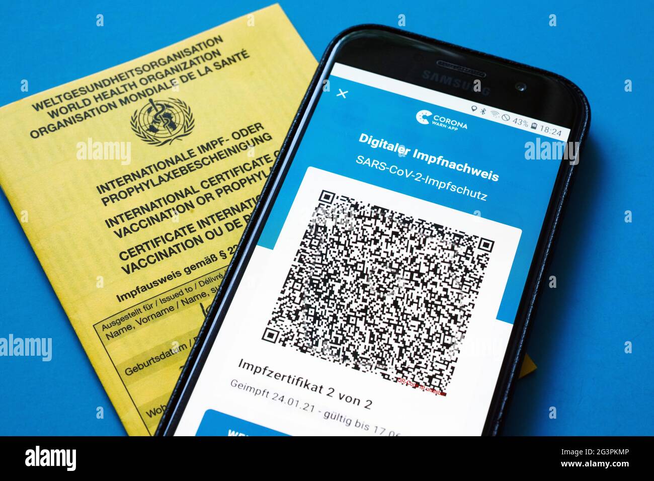 QR-Code, das digitale Impfzertifikat in der Corona Warn-App auf einem Smartphone bestätigt eine abgeschlossenen Impfung gegen Covid-19. Liegt auf der gelben Internationalen Impfbescheinigung, Impfpass. - ACHTUNG! QR-Code und persönliche Angaben sind unkenntlich gemacht! Stock Photo