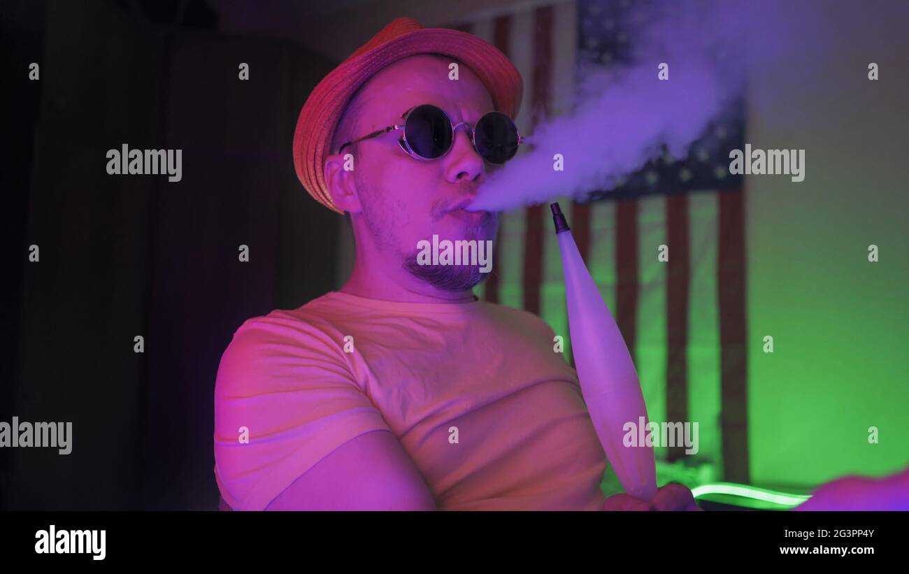 Hipster Exhales A Cloud Of Smoke Smoking A Hookah In Neon Lights Stock Photo