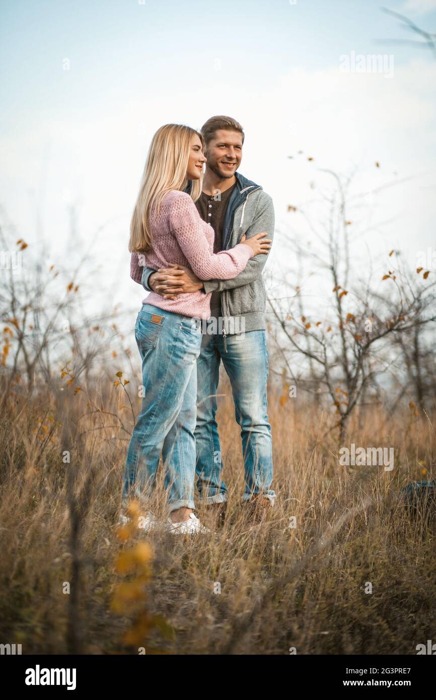 Hugging couple smiling standing on autumn grass outdoors, young guys cuddling in nature against a blue sky Stock Photo