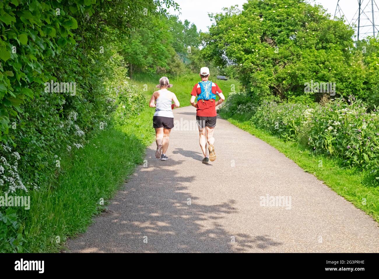 Two older people couple rear back view runners running jogging along Walthamstow Wetlands path in spring countryside 2021 London N17 UK KATHY DEWITT Stock Photo