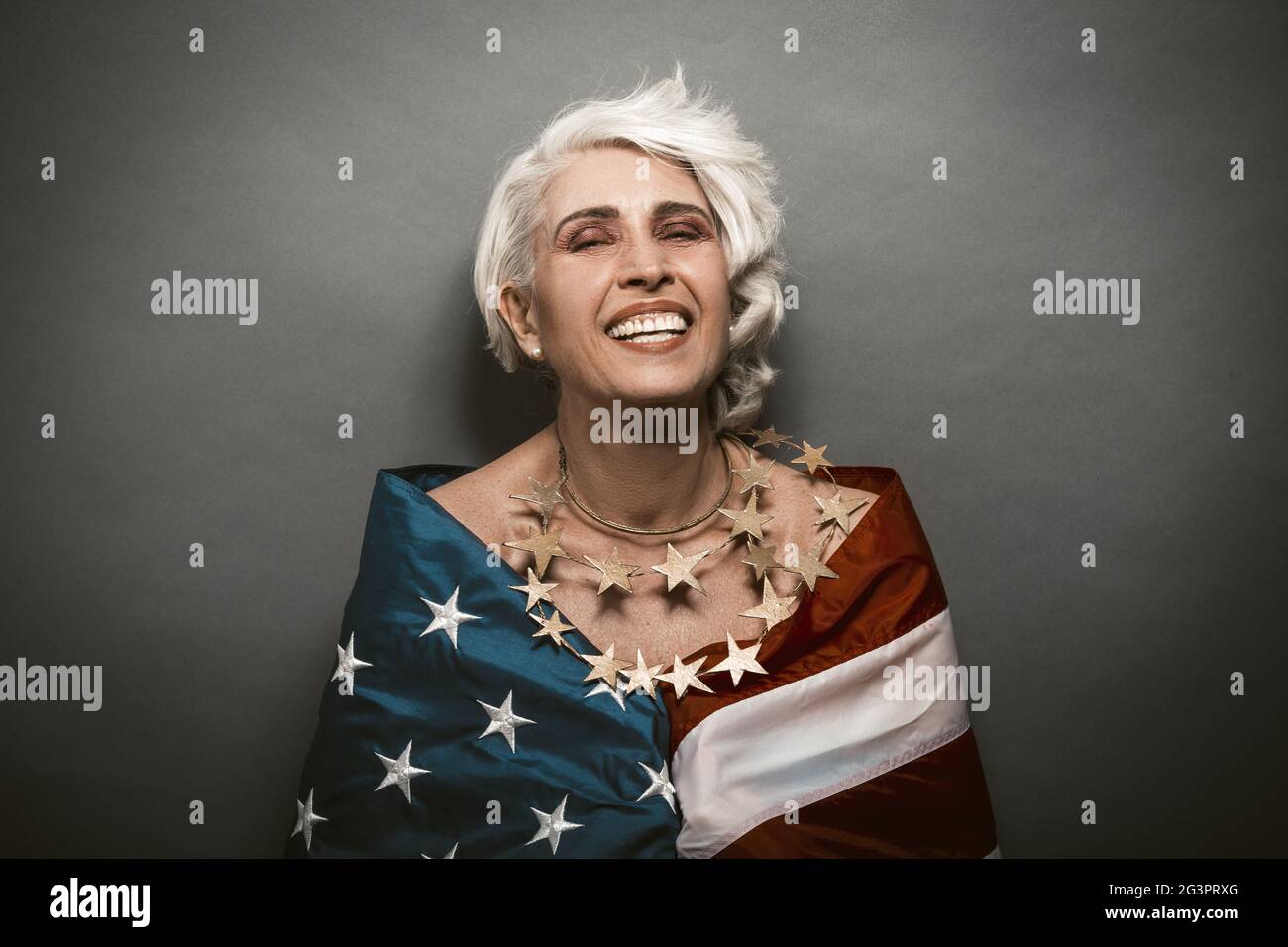 Toothy smiling senior woman covered with American flag Stock Photo