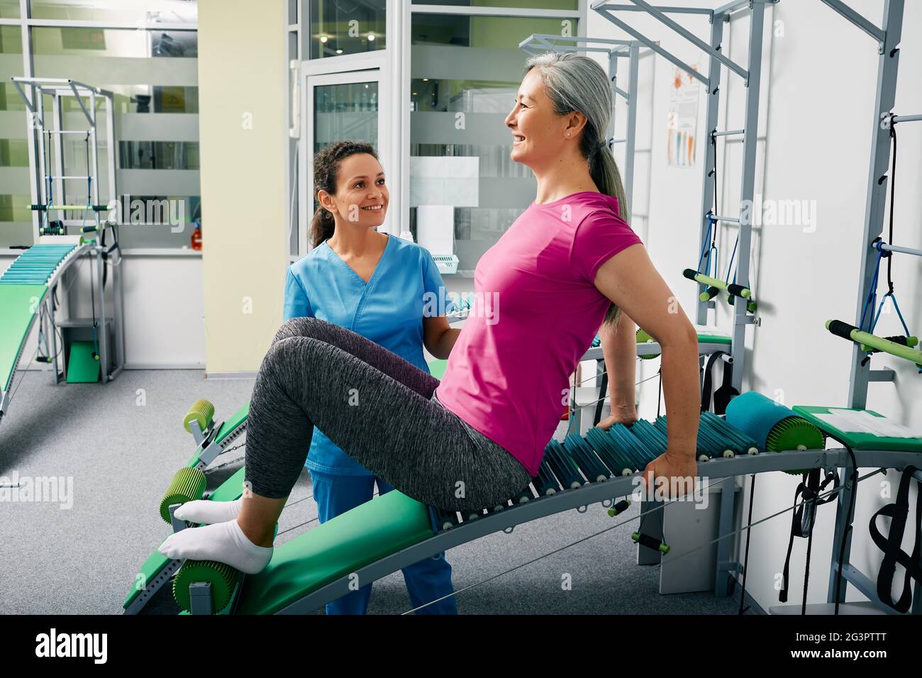 Woman recovering from a lumbar spine injury in a rehabilitation center while sitting on special recovery table with her physiotherapist Stock Photo