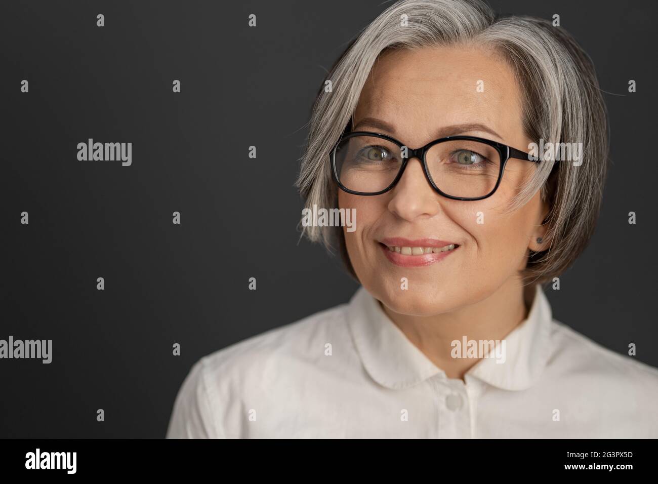 Pretty gray-haired woman in white shirt. intelligent middle-aged businesswoman in glasses with medium length care hairstyle smil Stock Photo