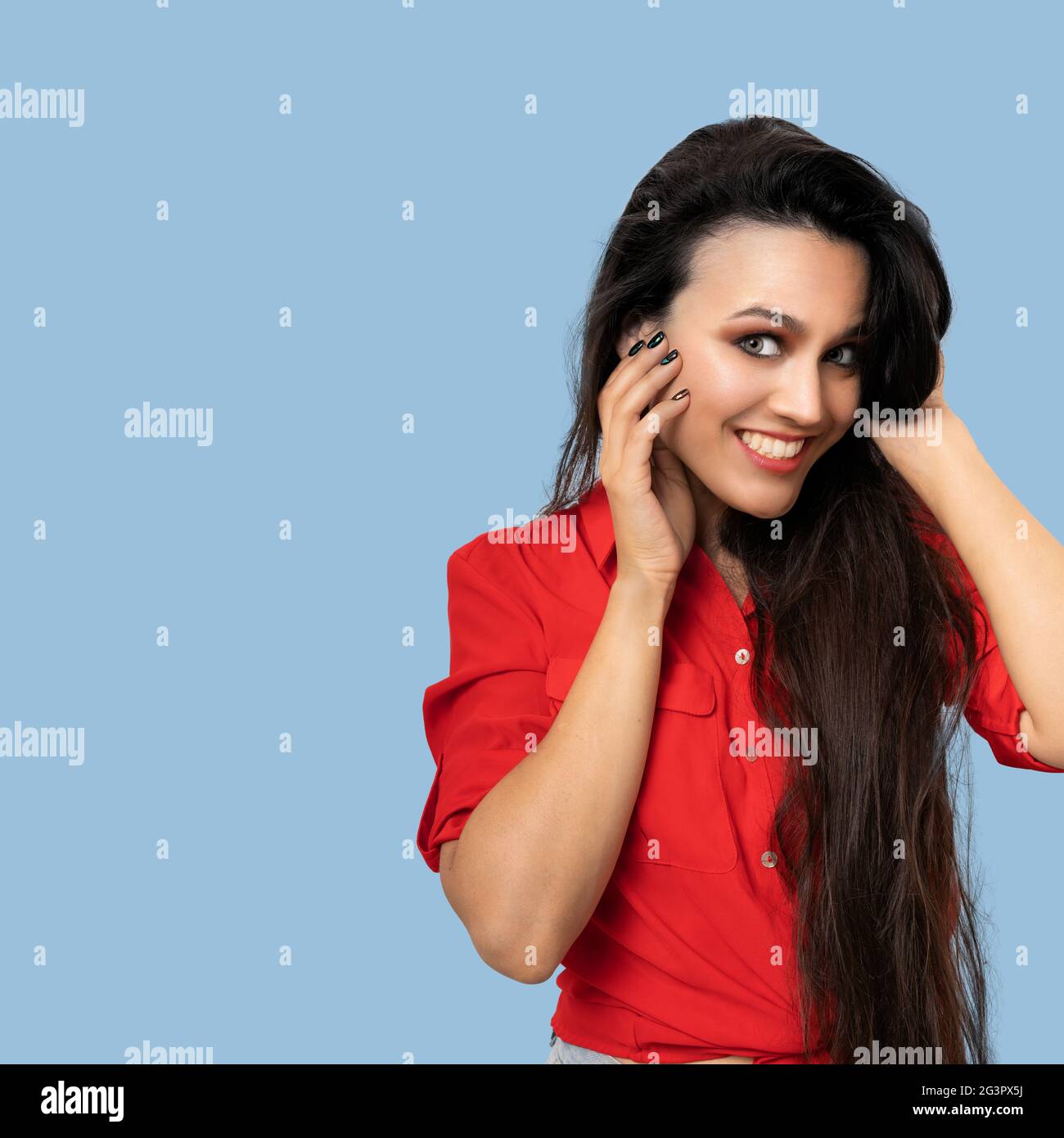 Toothy smiling woman touching face with hands while looking at camera. Side view of pretty young brunette in a red blouse posing Stock Photo