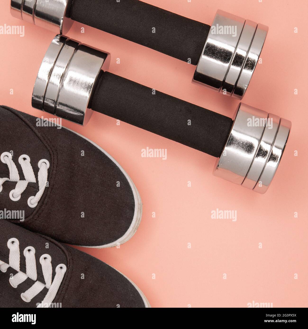 Metal small dumbbells and sneakers for training on a pink background. Stock Photo