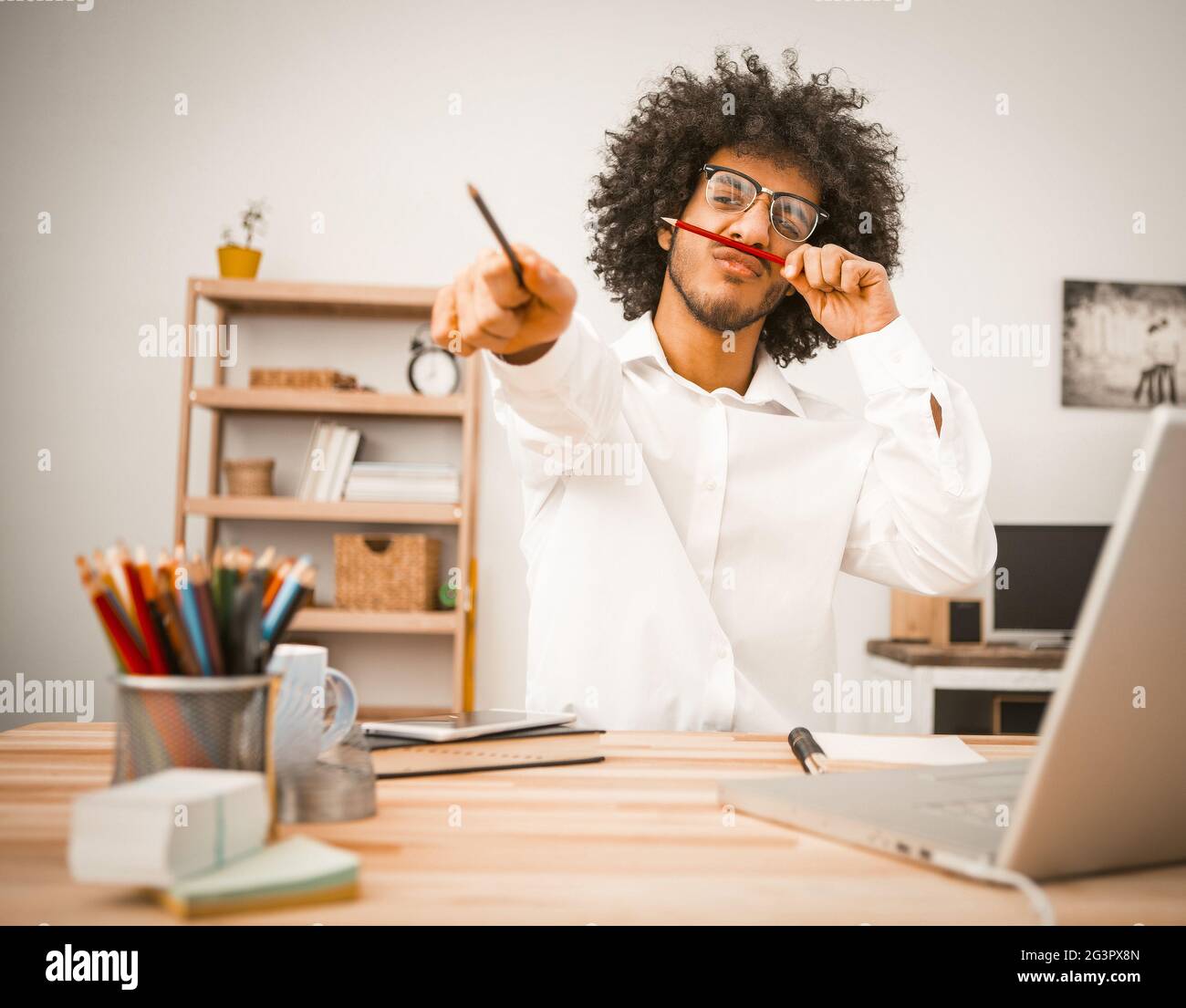 Creative man takes a break from work. Millennial guy having fun making a mustache by applying a pencil under his nose.businessma Stock Photo