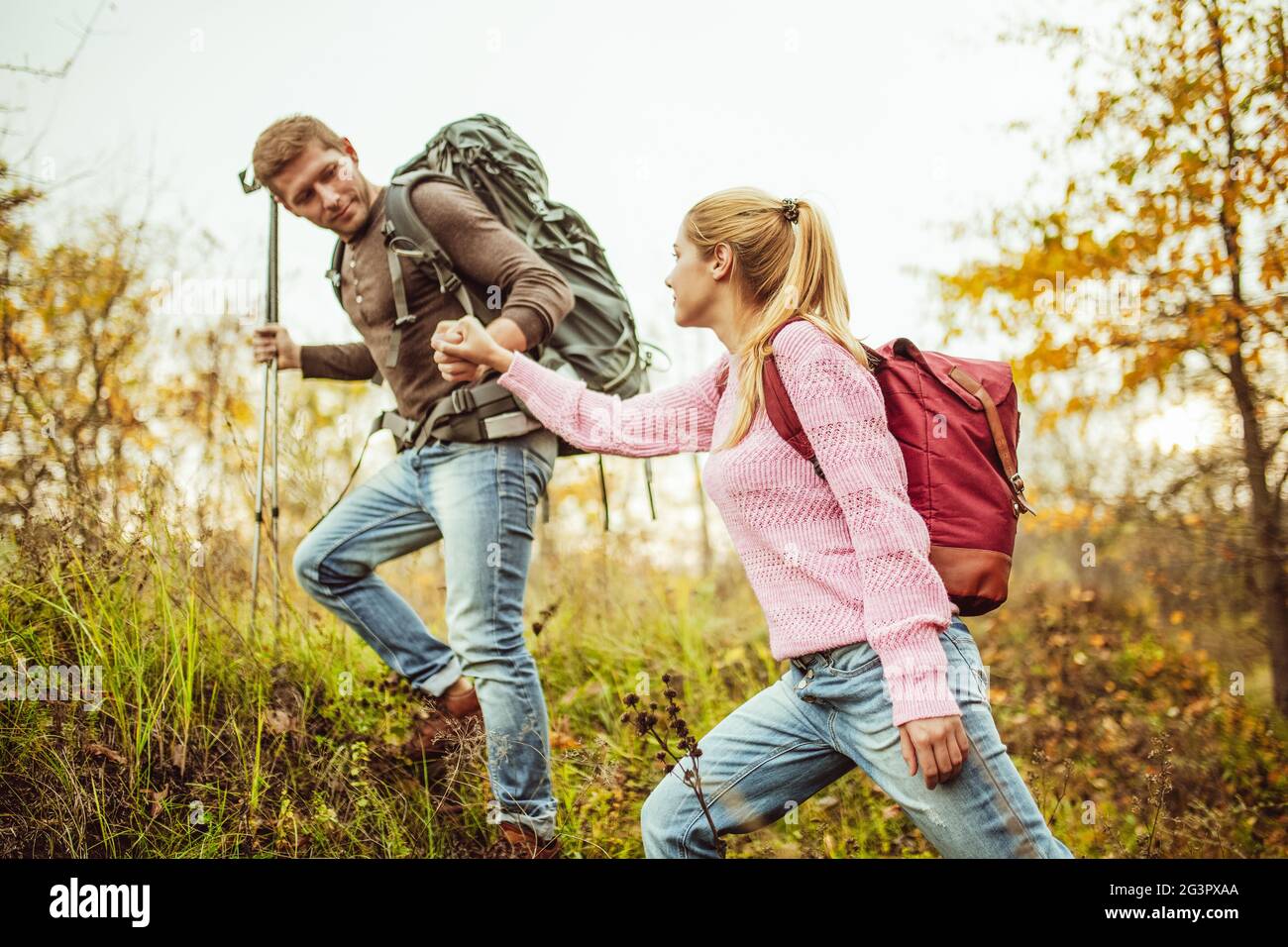 Man helps a woman climb a hill holding woman's hand and hiking poles in other hand. Hiking concept. Support and assistance conce Stock Photo
