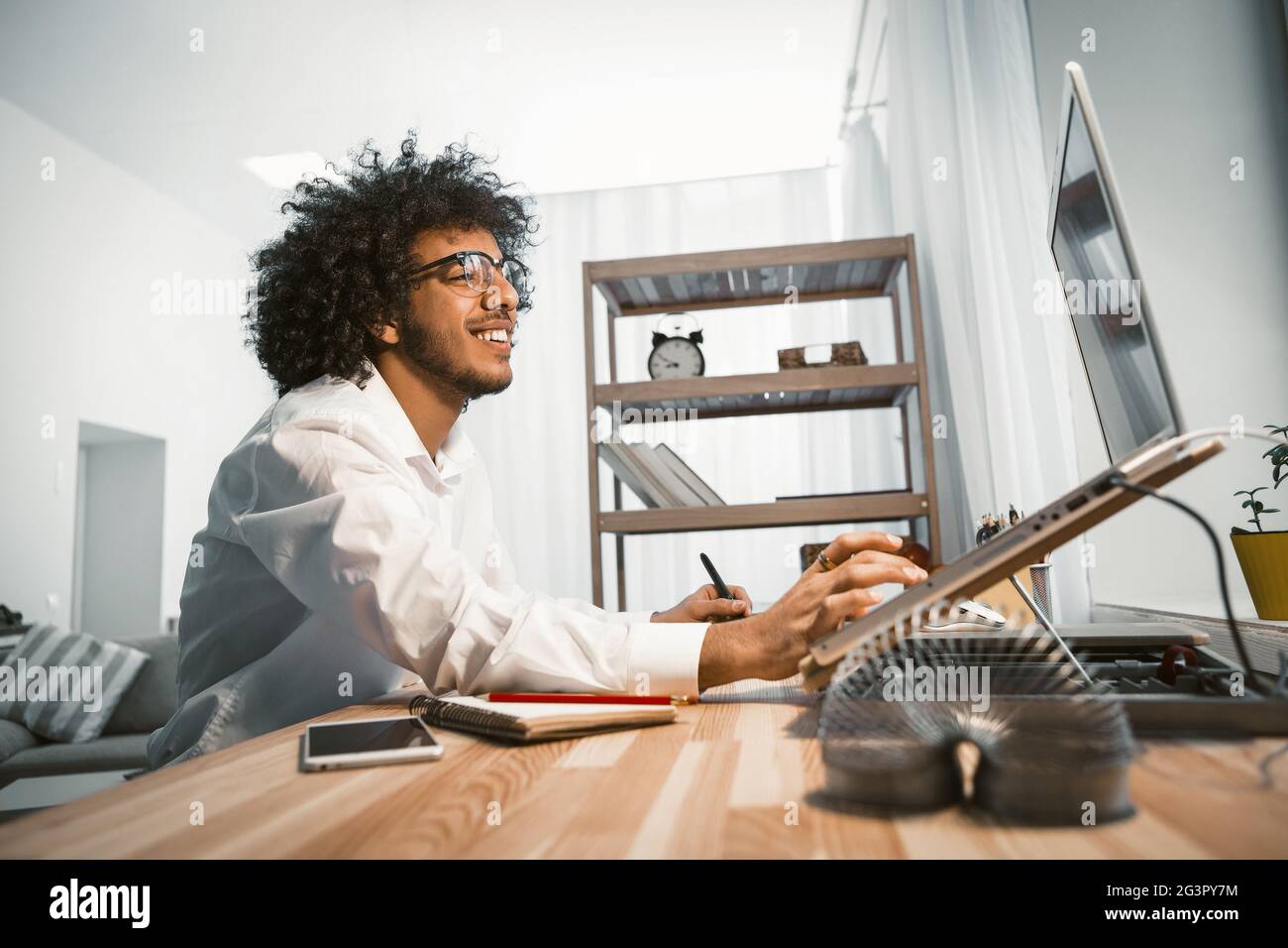 Inspired designer working on computer with new project. Young freelance man works on laptop sitting at home workplace. Side view Stock Photo