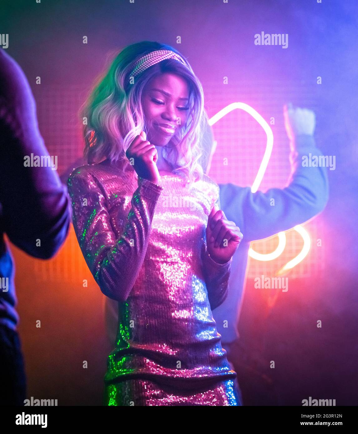 Happy African girl dancing in night club. Pretty African American woman having fun bright neon glowing. Night life concept. Ente Stock Photo