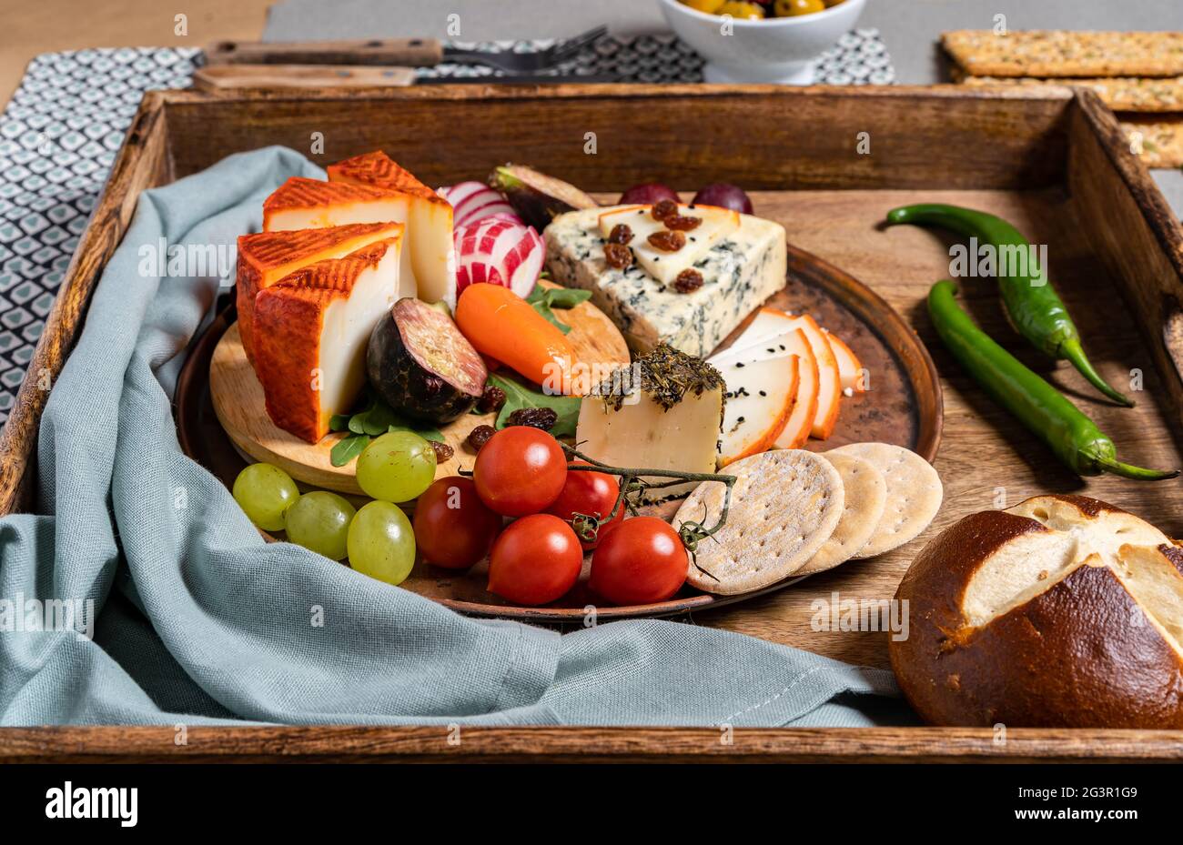 Food photography of cheese board on a wooden tray with olives, crackers, cherry tomatoes, asparagus and peppers stuffed with cream cheese. Mediterrane Stock Photo