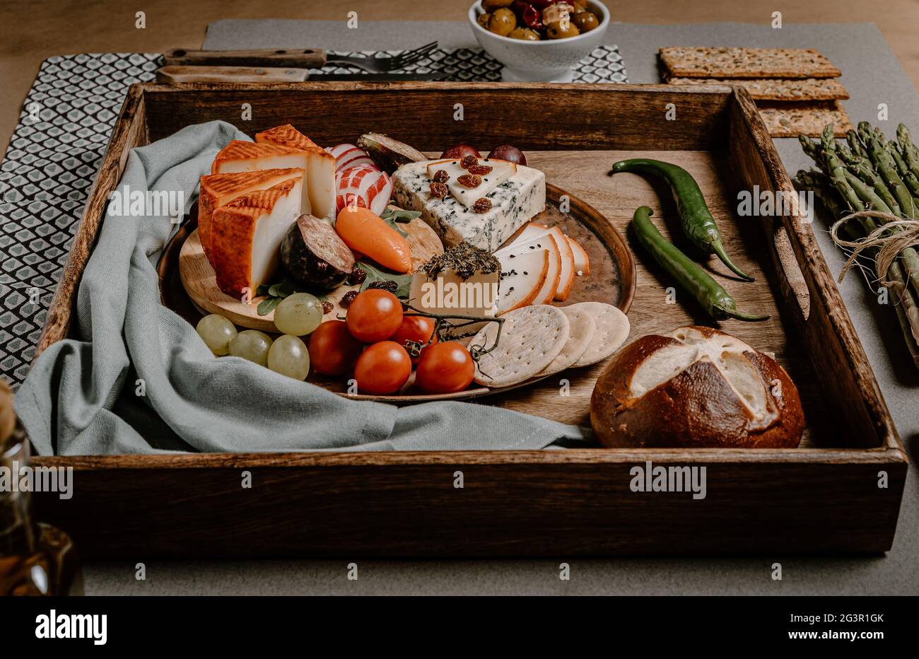 Food photography of cheese board on a wooden tray with olives, crackers, cherry tomatoes, asparagus and peppers stuffed with cream cheese. Mediterrane Stock Photo