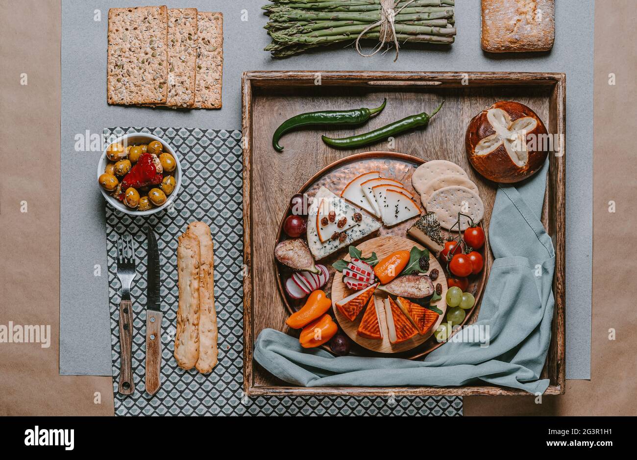 Food photography of cheese board with olives, crackers, cherry tomatoes, asparagus and peppers stuffed with cream cheese on a wooden tray. Mediterrane Stock Photo