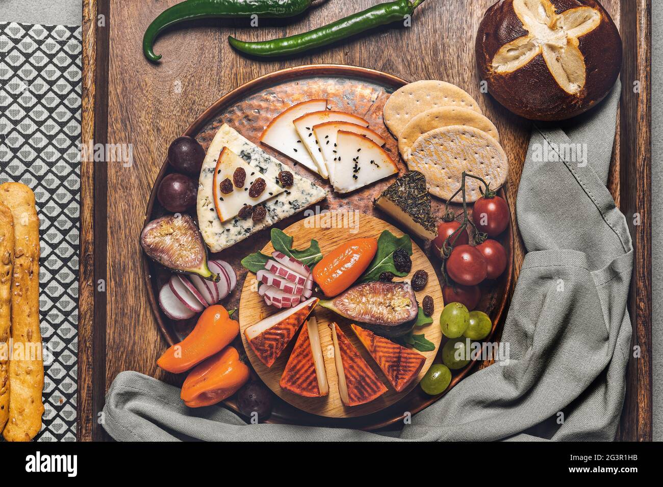 Food photography of cheese board with olives, crackers, cherry tomatoes, asparagus and peppers stuffed with cream cheese on a wooden tray. Mediterrane Stock Photo