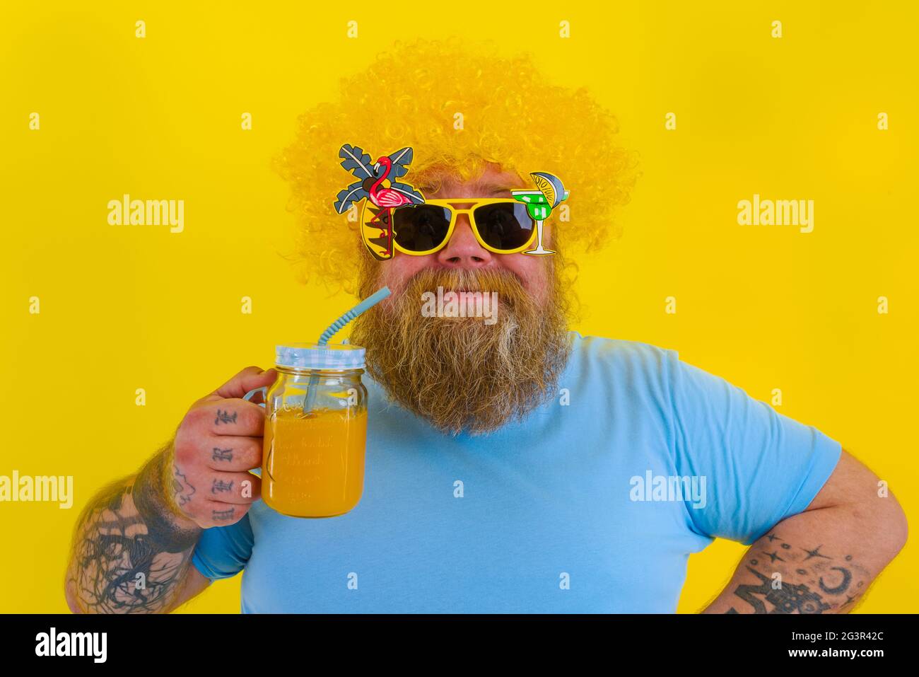 Fat happy man with wig in head and sunglasses drinks a fruit juice Stock Photo