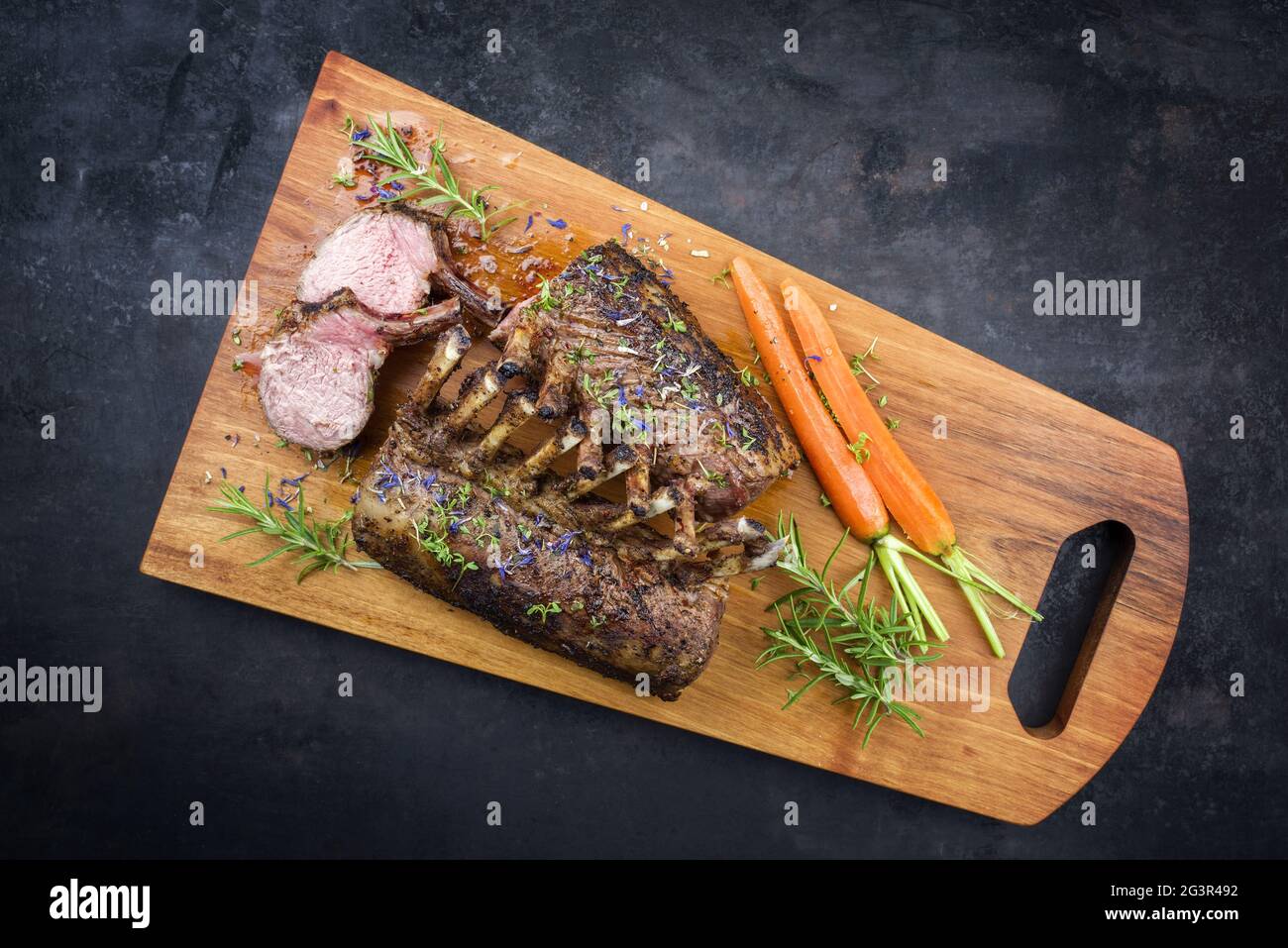 Barbecue rack of lamb with carrot and herbs offered as top view on a modern design wooden board with copy space Stock Photo