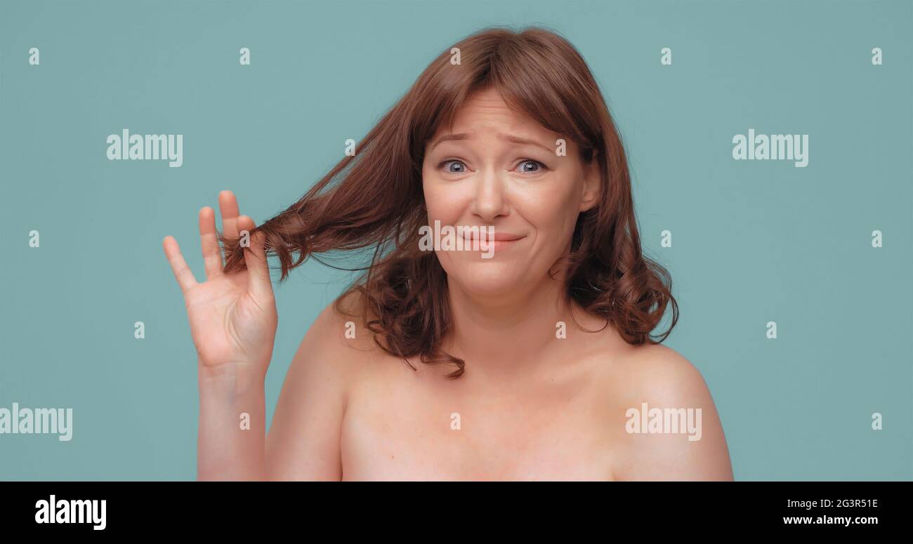 Unhappy caucasian woman holds ends of hair looking at camera. Sad beautiful lady need hair care having problem with her hairstyl Stock Photo