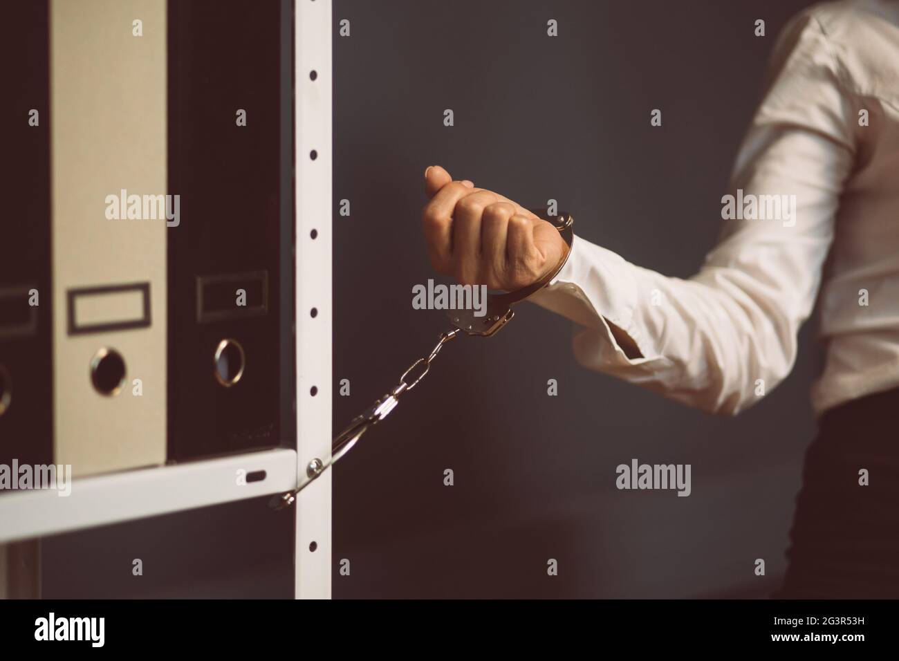 Businesswoman locked in office. Female hand handcuffed to office bookcase with folders. Lock down concept. Close up shot. Tinted Stock Photo