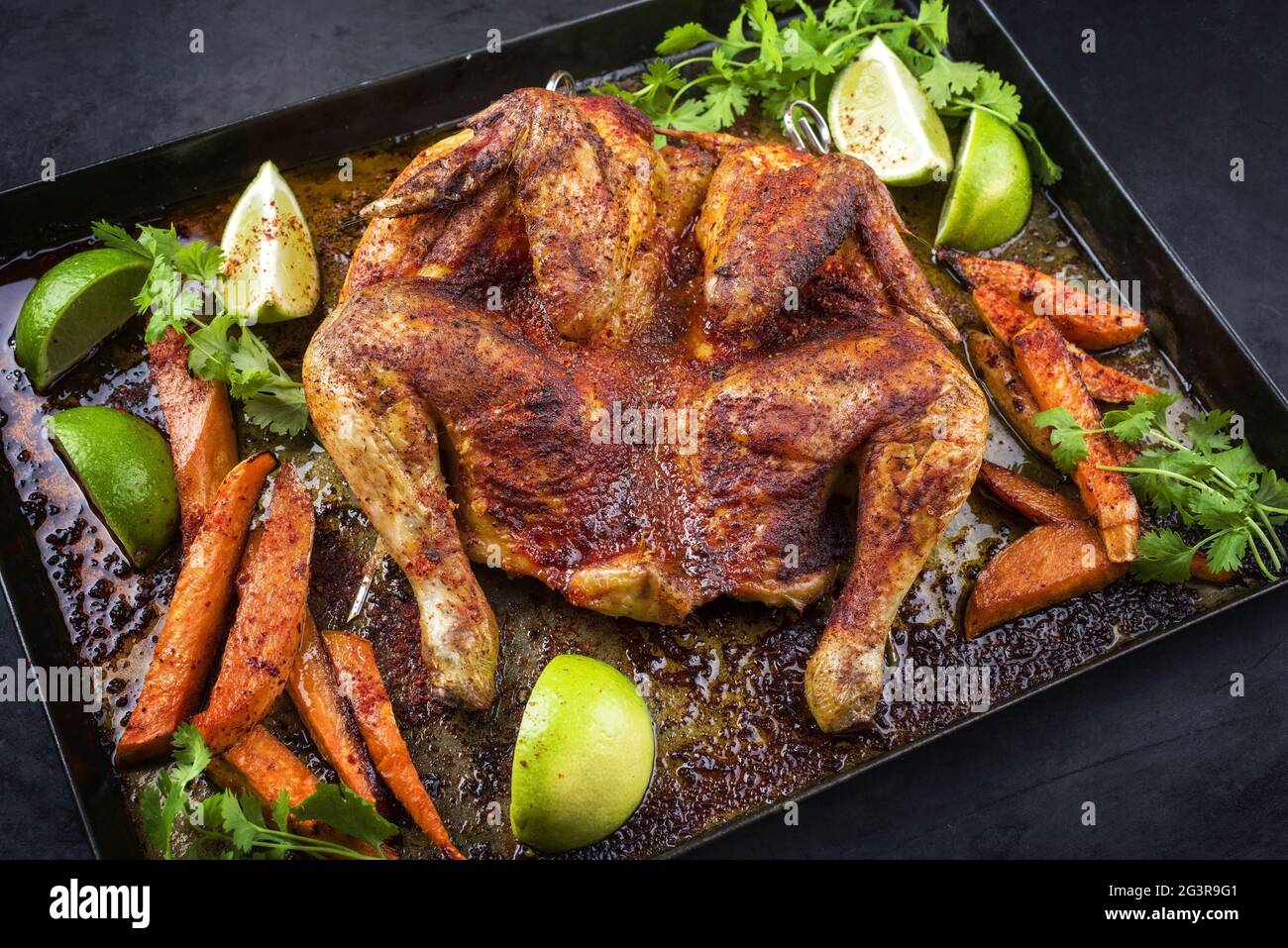 Traditional barbecue spatchcocked chicken al mattone chili with sweet potato chips and limes offered as close-up on an old rusti Stock Photo