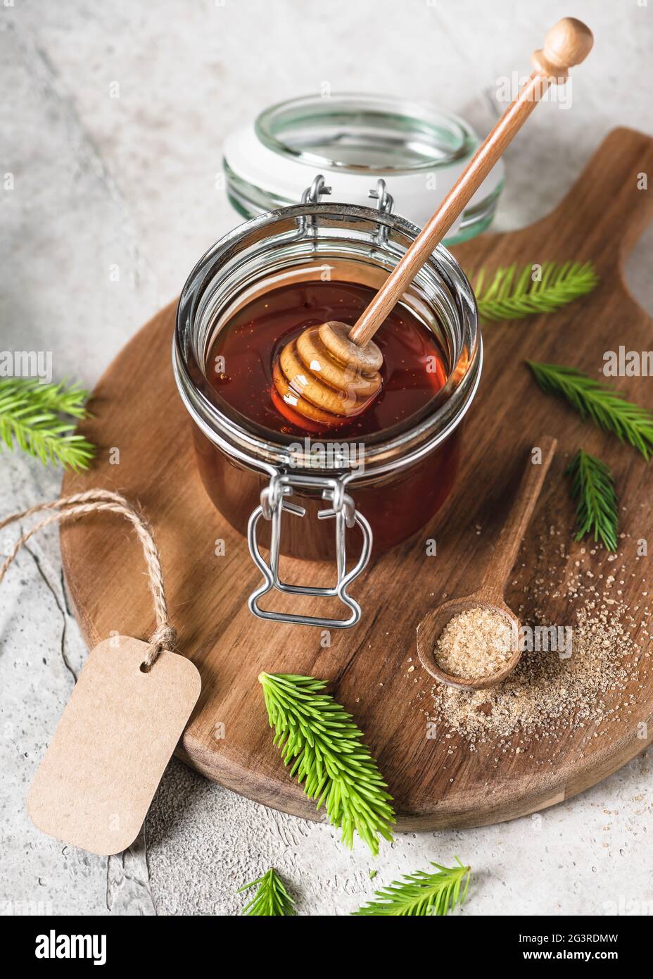 Jar of homemade jam from young fir buds, needles and nature sugar with wooden honey spoon. Making spruce tips jam at home. Stock Photo