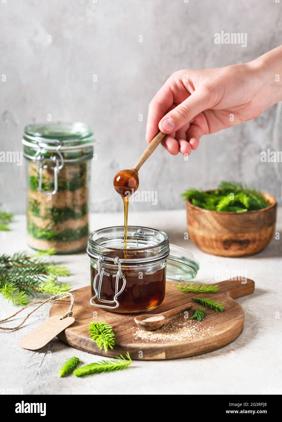 Hand holding a wooden spoon with flowing homemade honey made from young green spruce tips and nature sugar. Stock Photo