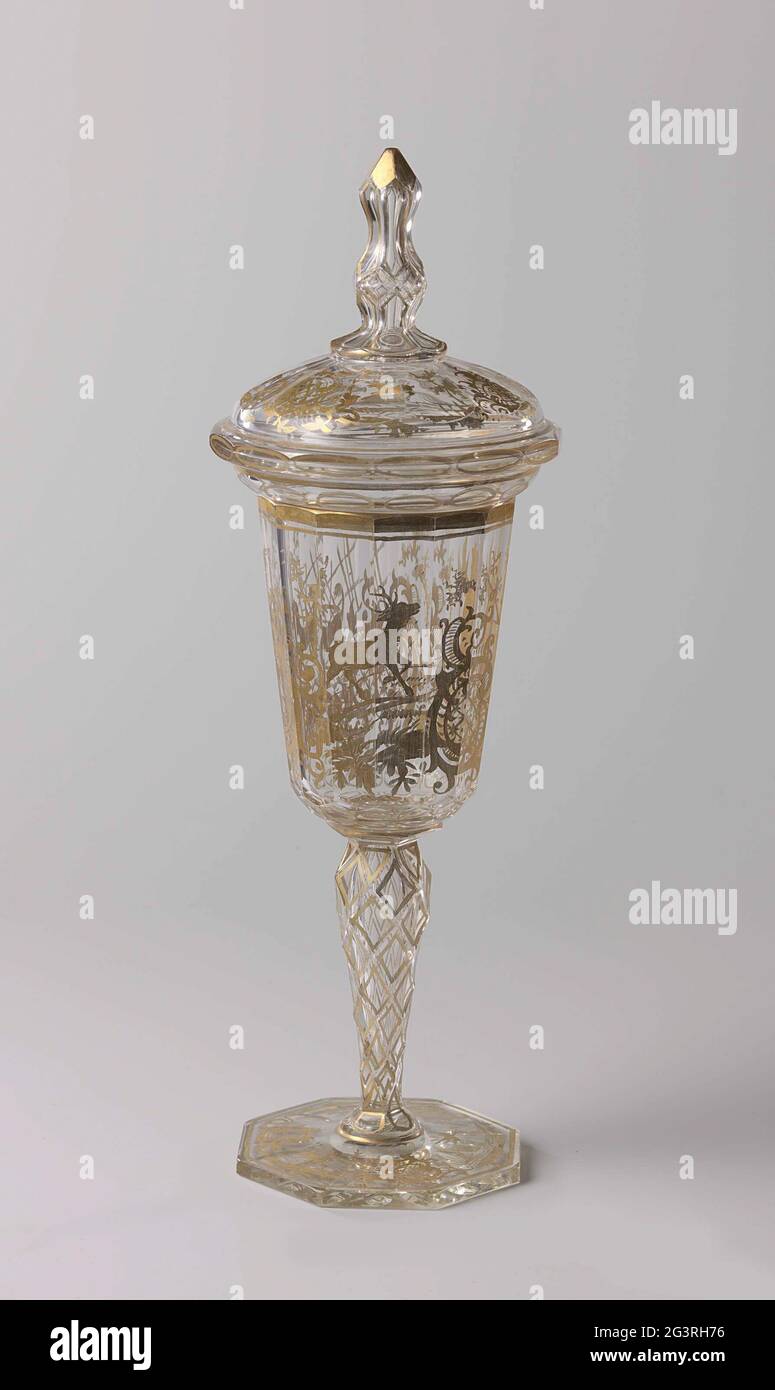 Cup with lid, with a yacht scene. Flat, octagonal, facet cut foot. Facet cut, baluster-shaped strain. Funnel-shaped, rounded and faceted chalice. Vaulted, faceted lid with overrunning edge and a facet cut, baluster-shaped button, ending in a point. On the chalice, in Neo-Louis XV style, a yacht scene with a hunter with a shot duck in gold. At the foot and the lid a deer, a stork and a dog surrounded by Rocaille ornament. The facets on foot, trunk and knob dipped off with gold. Stock Photo